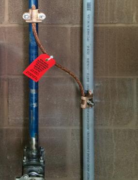 The lightning protection down conductor (enclosed in PVC conduit on the right) is bonded to the adjacent metal plumbing pipe.